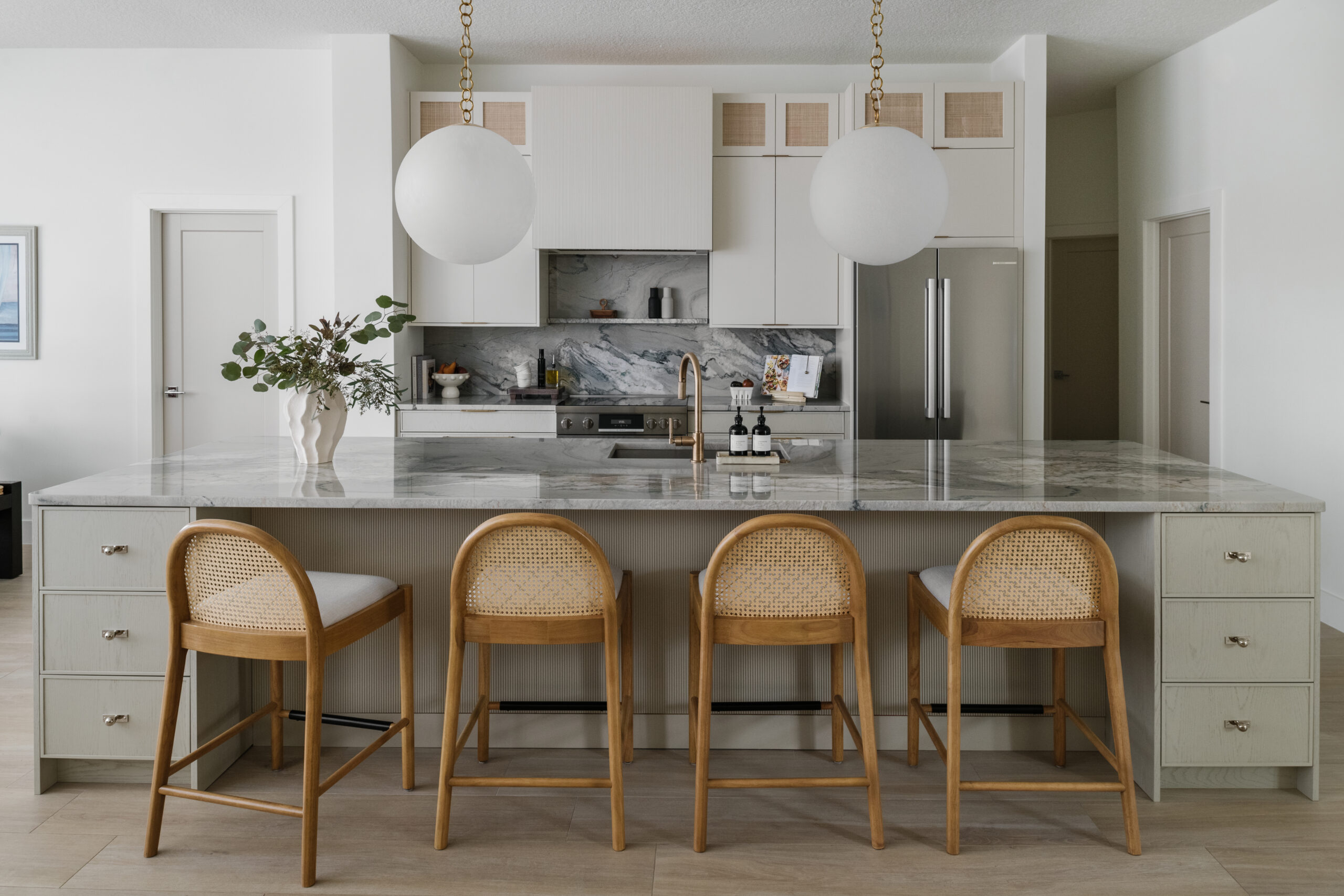 Neutral contemporary kitchen with oversized globe pendants, quartzite countertops with full stone backsplash and huge island