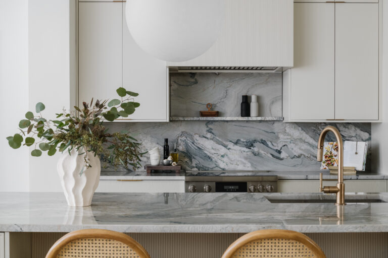 Detail of cooking range elevation with full height quartzite backsplash with ledge, slatted range hood, brass hardware and fixtures .