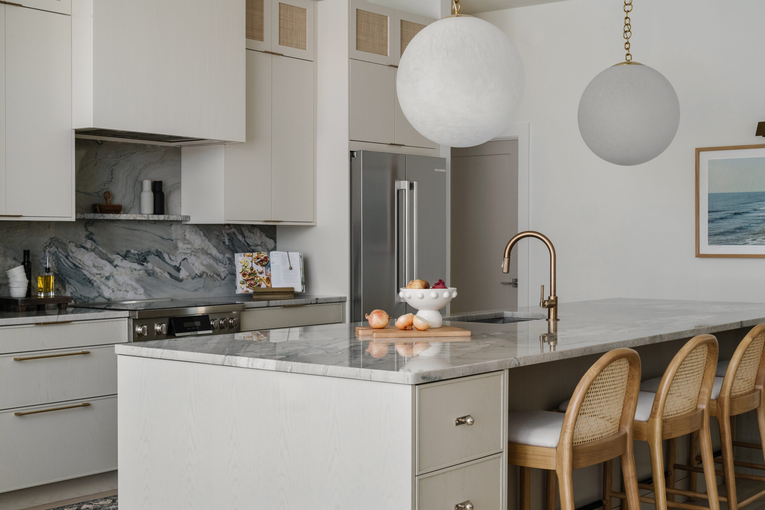 Angled kitchen view showing large island, cooking range and oversized globe pendants.