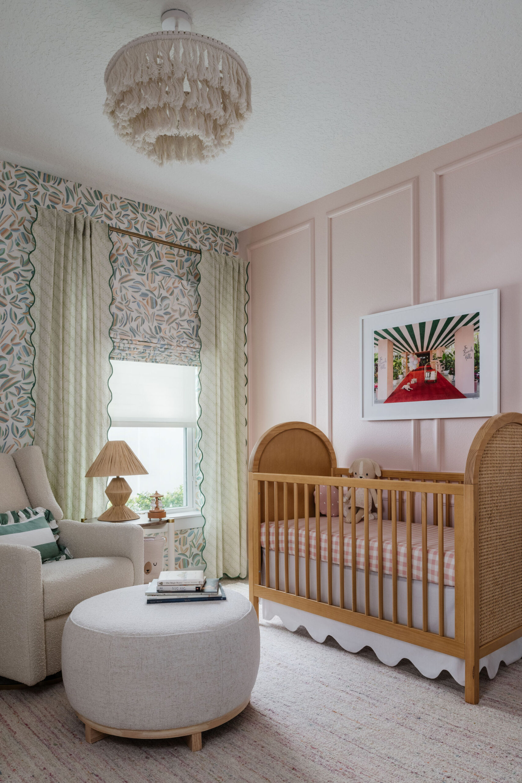 girl nursery with wallpaper walls, crib, artwork, ottoman and fringe light fixture